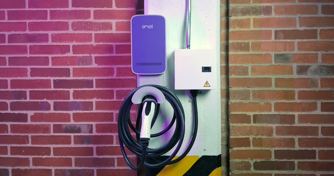 Cargador de pared Enel para vehículo eléctrico con manguera enrollada, instalado junto a su caja de protección eléctrica