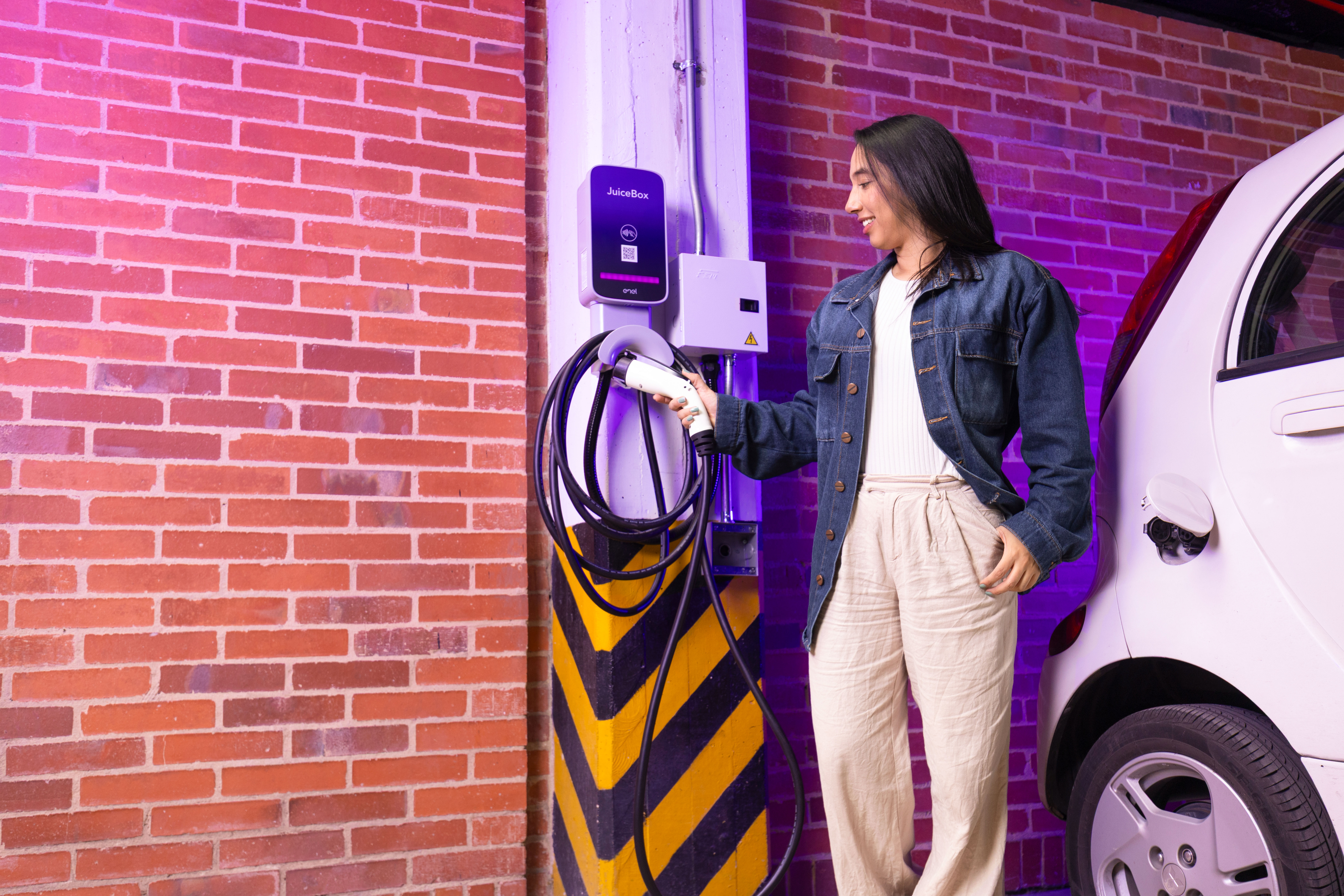 Mujer toma el conector de un cargador JuiceBox de Enel instalado en la pared de un garaje residencial