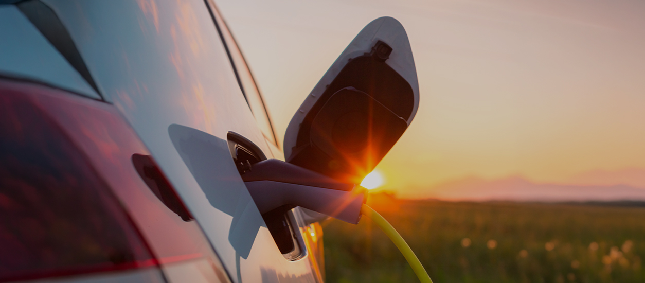 Conector de carga enchufado en el puerto de un vehículo eléctrico al atardecer
