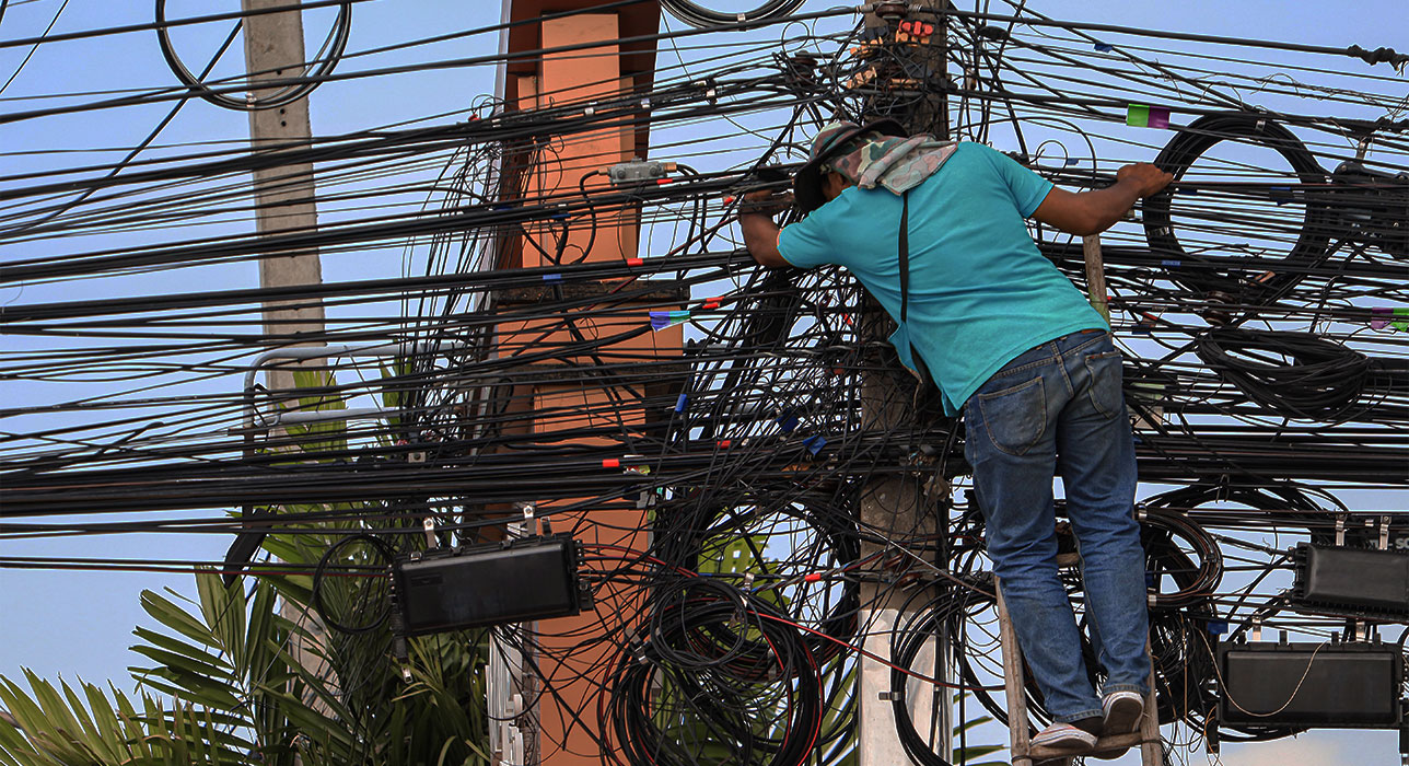 Hombre manipulando cables en un poste, corriendo riesgos eléctricos.