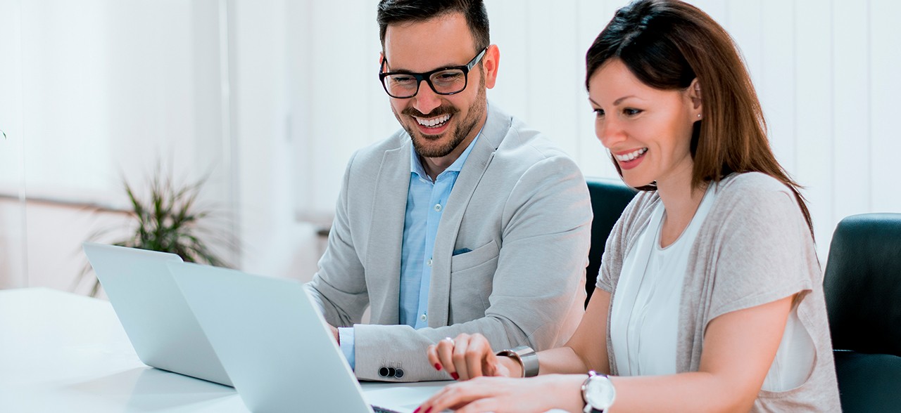 Smiling corporate man and woman looking at laptops during a business meeting in a bright office.