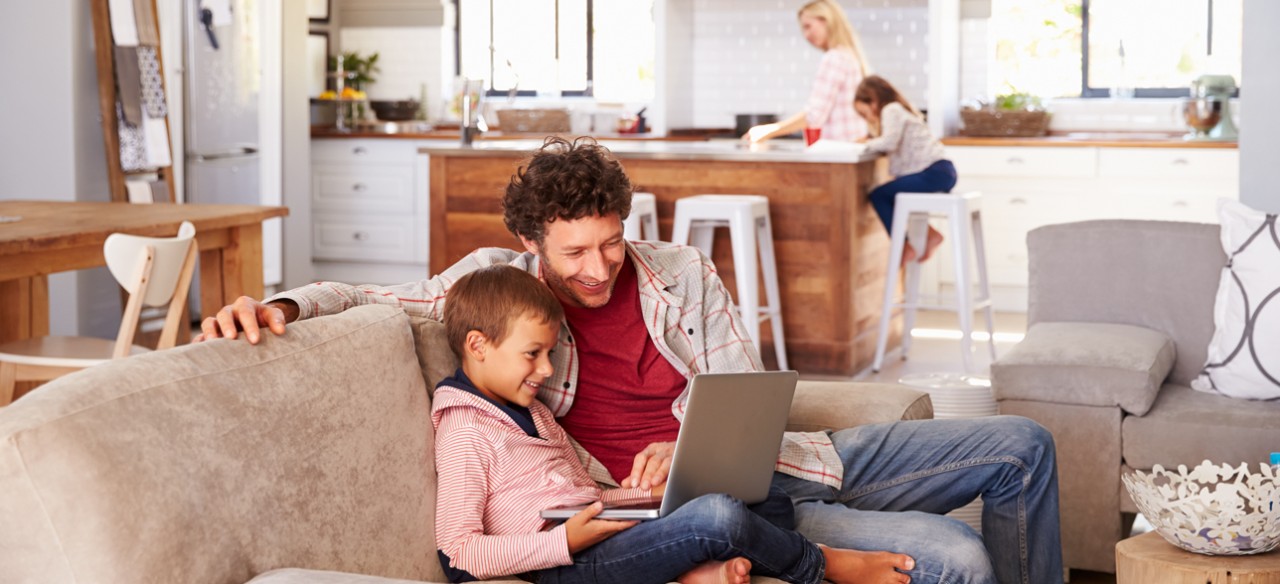 Padre e hijo usan un computador portátil en casa, representando el uso responsable de la energía.