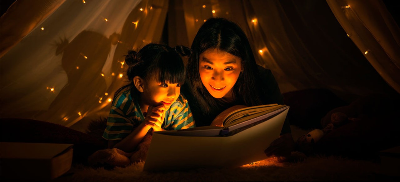 Madre e hija leyendo un cuento sobre los riesgos eléctricos, dentro de una carpa de juegos.
