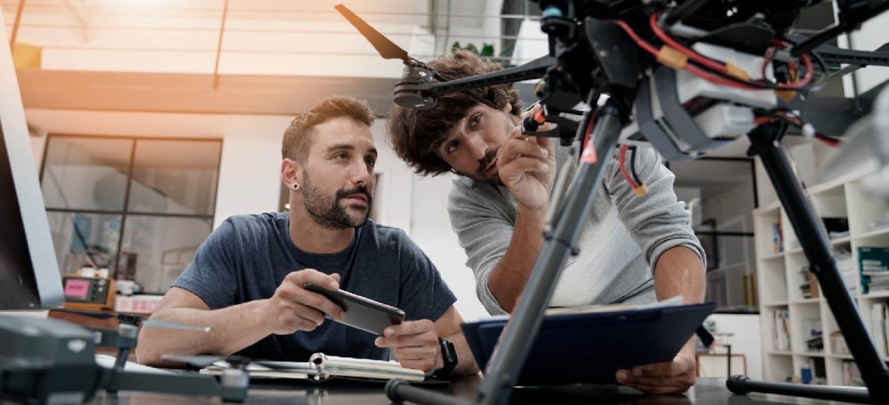 Dos jóvenes trabajando juntos en ideas de innovación con drones en una oficina.