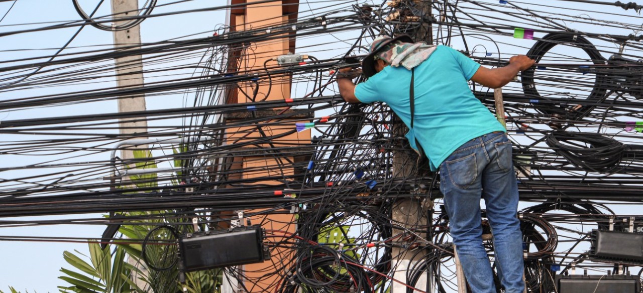 Hombre manipulando cables en un poste, corriendo riesgos eléctricos.
