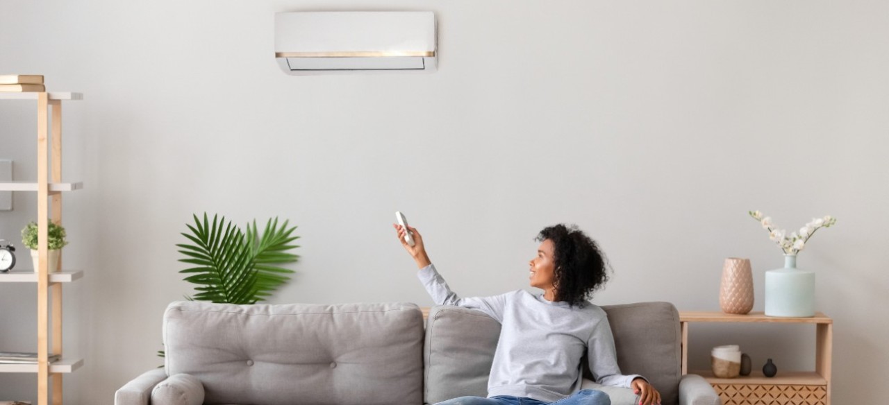 Mujer sentada en un sofá, encendiendo el aire acondicionado, porque puede acceder a los servicios de luz.