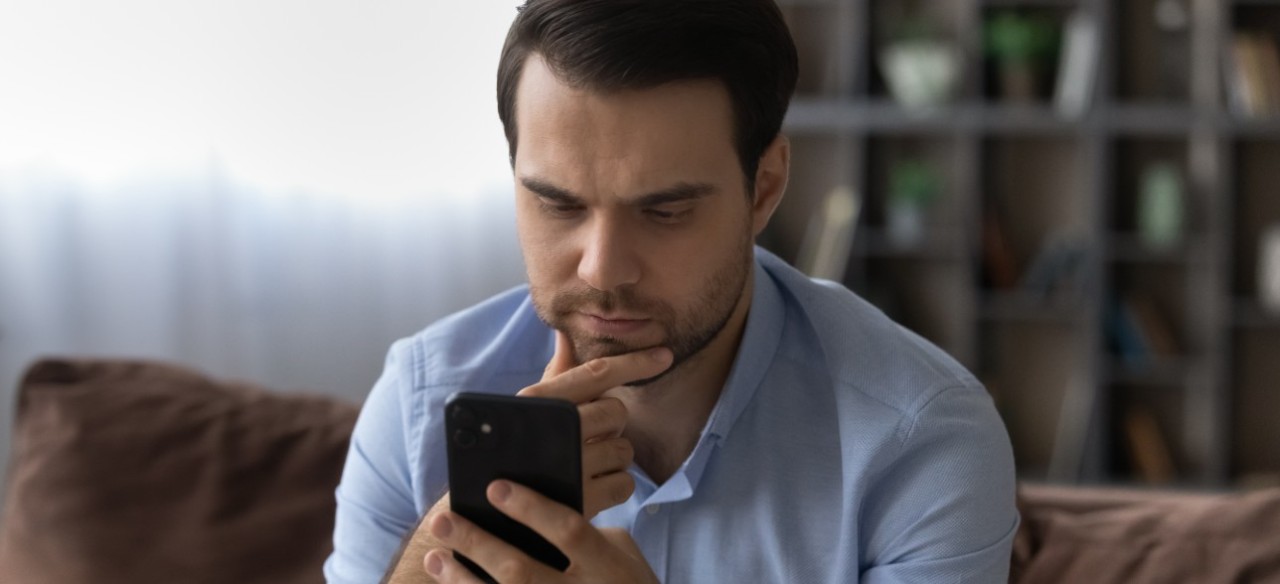 Hombre preocupado mirando su celular para ver cómo denunciar el hurto de energía eléctrica.