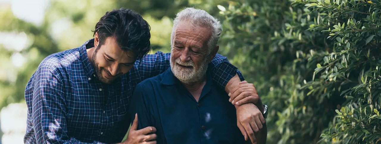 Padre e hijo paseando por un parque abrazados, después al revisar las características del plan de Asistencia Funeraria de Enel