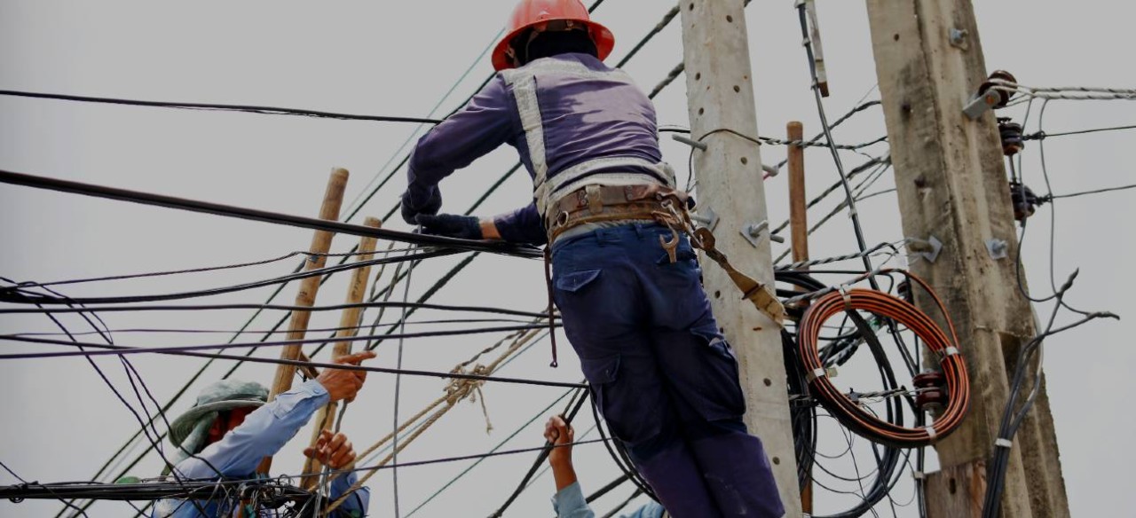 Trabajadores realizando mantenimiento en un poste con redes de energía y telecomunicaciones.