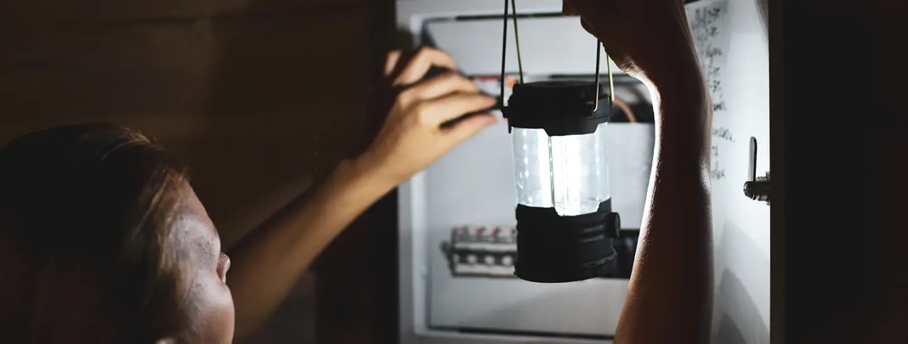 Mujer con una emergencia eléctrica en casa, revisando con linterna la caja de fusibles