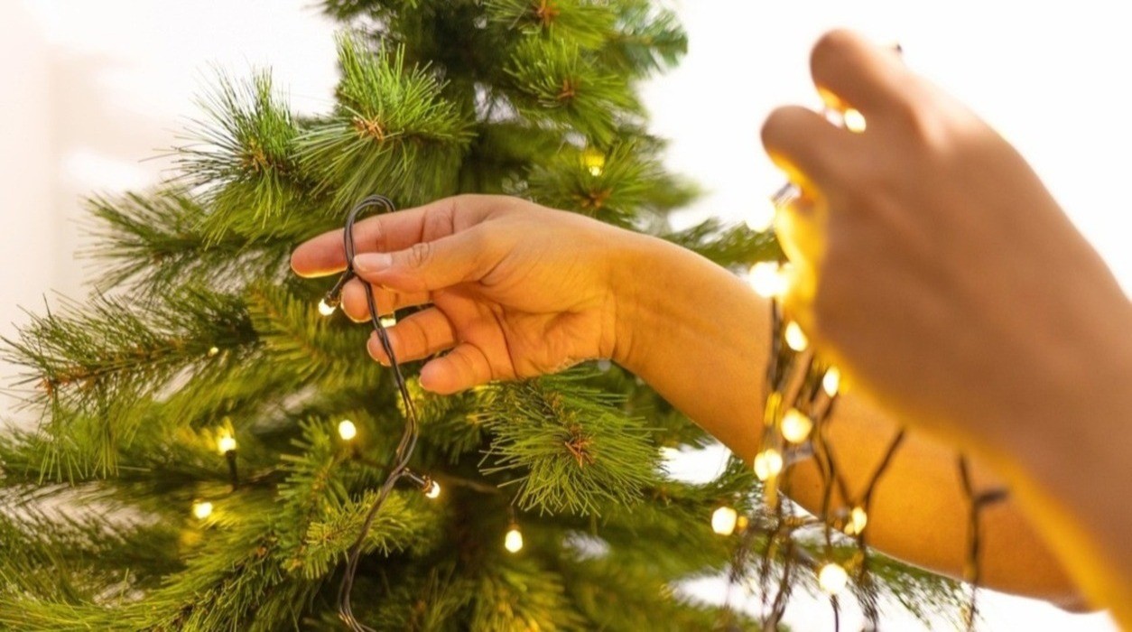 Persona instalando luces navideñas en un árbol de Navidad, mostrando una conexión segura y adecuada de los cables eléctricos. 