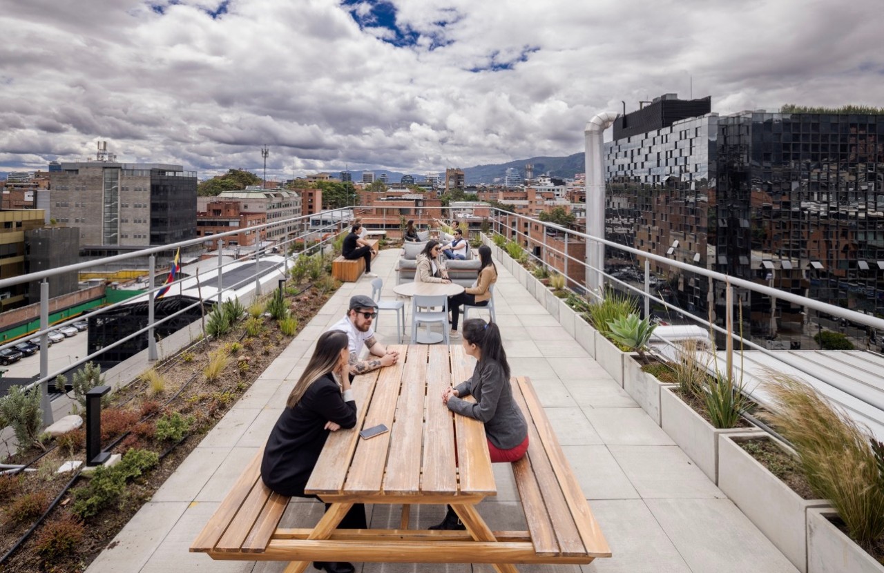 Colaboradores de Enel conversan en una terraza corporativa con vista urbana y montañas de Bogotá.