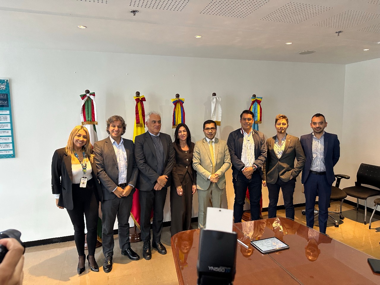 Ocho representantes de la alianza Áreas de Vida posan frente a banderas institucionales en una sala de reuniones