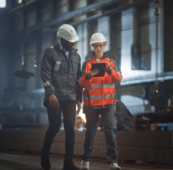 Dos ingenieros Usando Casco  chalecos en una obra revisando una tableta. Ilustra la conexión provisional de obra y riesgos eléctricos (RETIE)