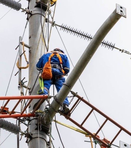 Técnico de Enel Colombia con arnés de seguridad realizando mantenimiento en poste de red eléctrica