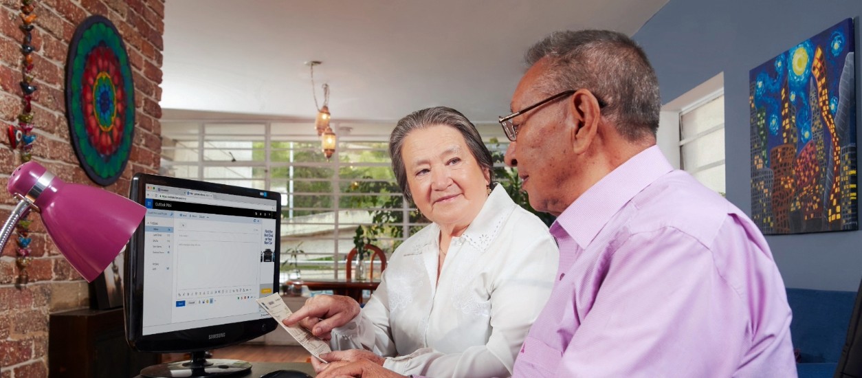 Cliente revisa su factura de energía en computador con asesoría en casa.