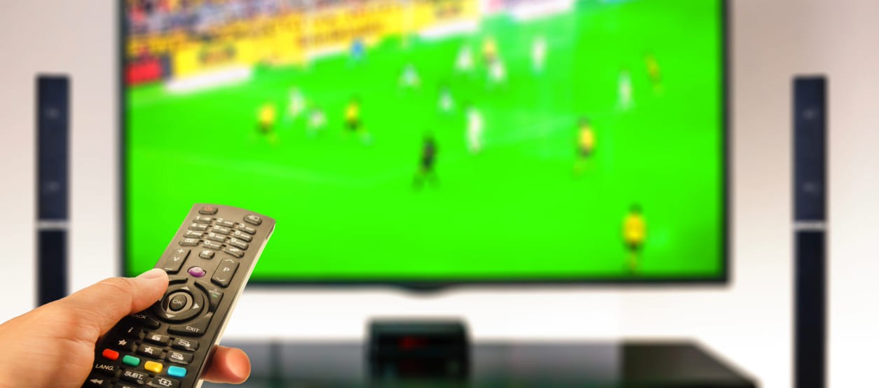 Persona usando un control remoto frente a un televisor durante un partido de fútbol en casa