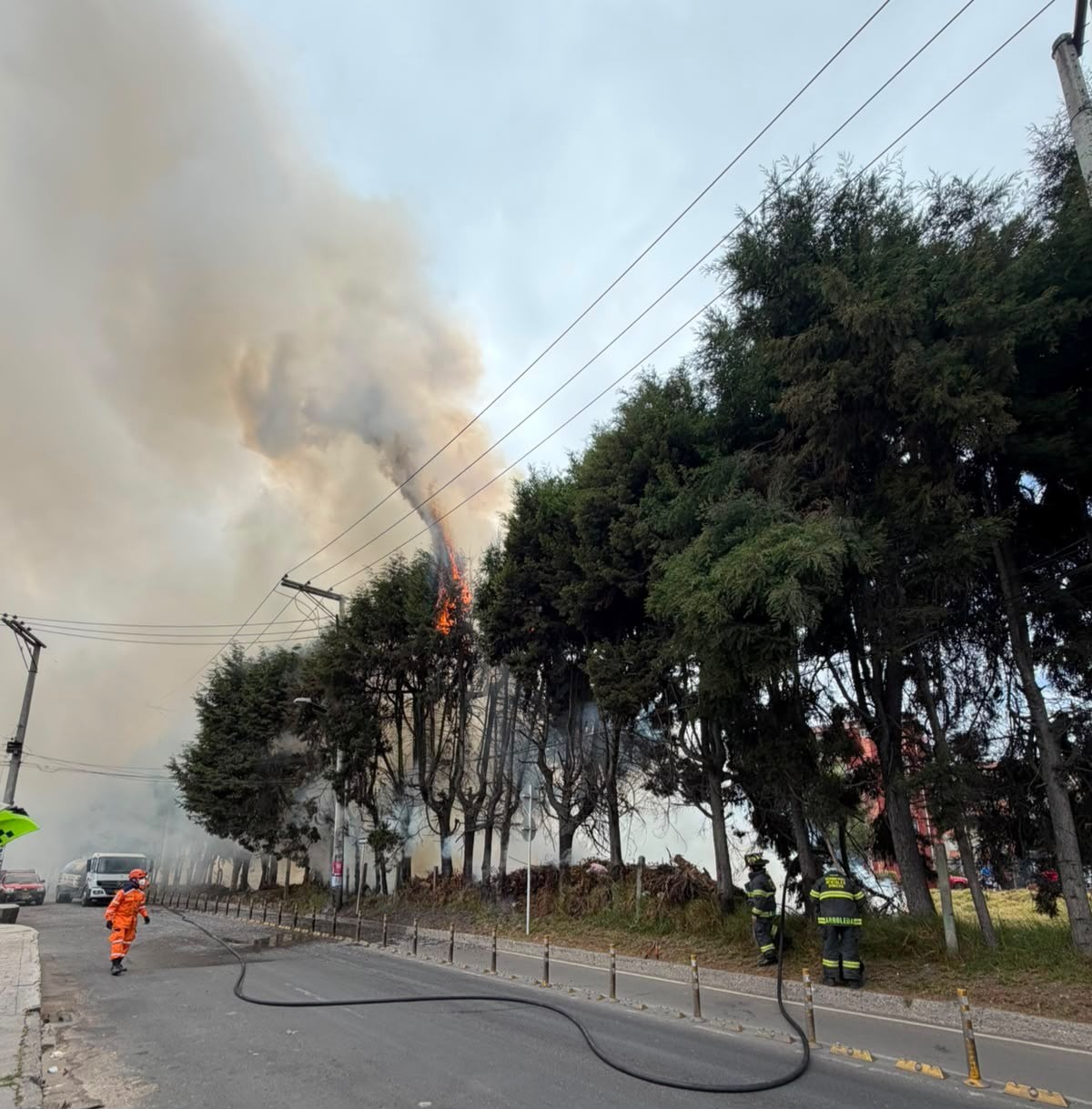 Personal de emergencia atendiendo un incendio forestal cerca de redes eléctricas e infraestructura en vía pública