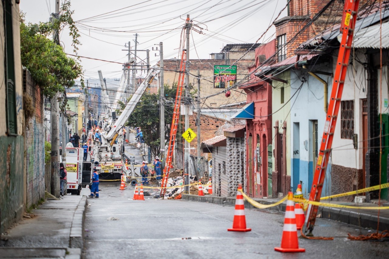 Técnicos de Enel Colombia reparan redes eléctricas en una calle de barrio señalizada con conos tras las fuertes lluvias