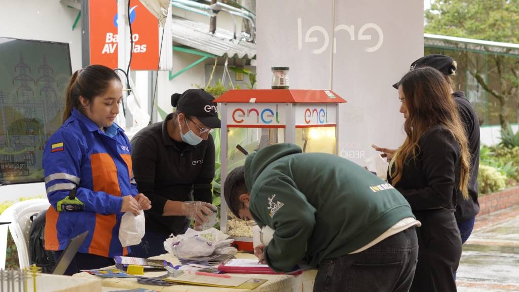 Colaboradora de Enel atiende a asistentes que diligencian información en el stand de la feria comunitaria