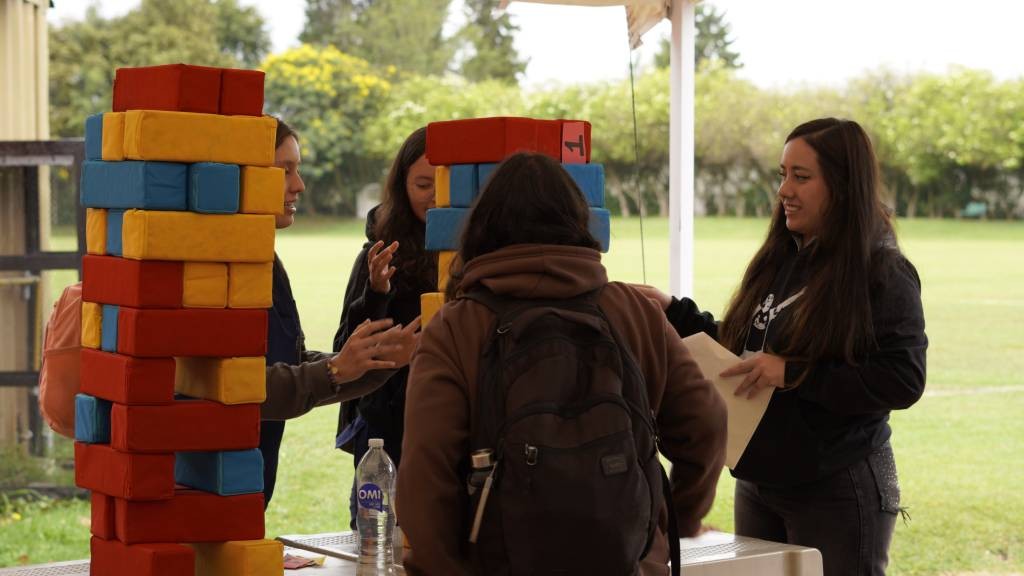 Participantes juegan con un bloque gigante de fichas de colores en una actividad al aire libre de la feria