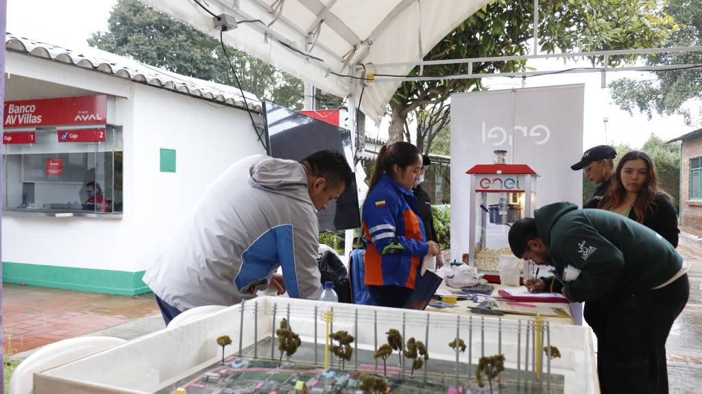 Colaboradores de Enel muestran una maqueta a visitantes en el stand de la feria comunitaria