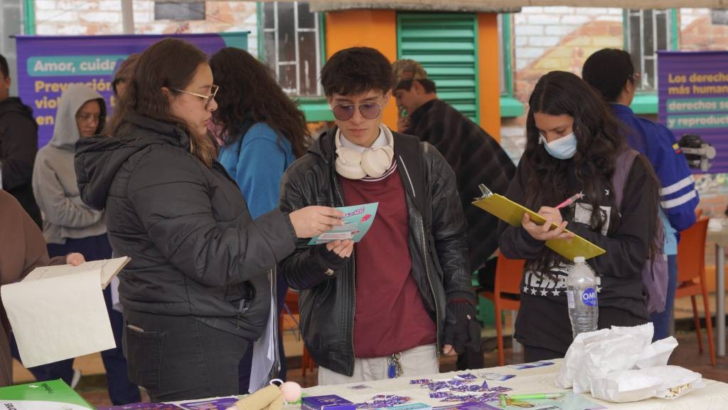 Jóvenes revisan material informativo en una mesa durante la feria de las comunidades cuidadoras