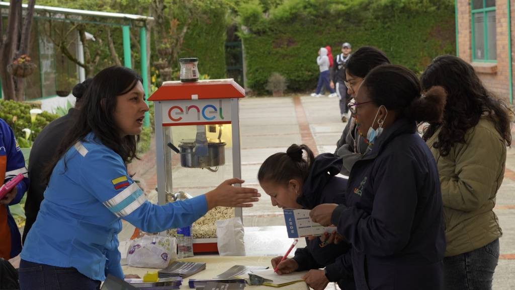 Colaboradora de Enel orienta a dos jóvenes que diligencian un formulario en el stand de la feria